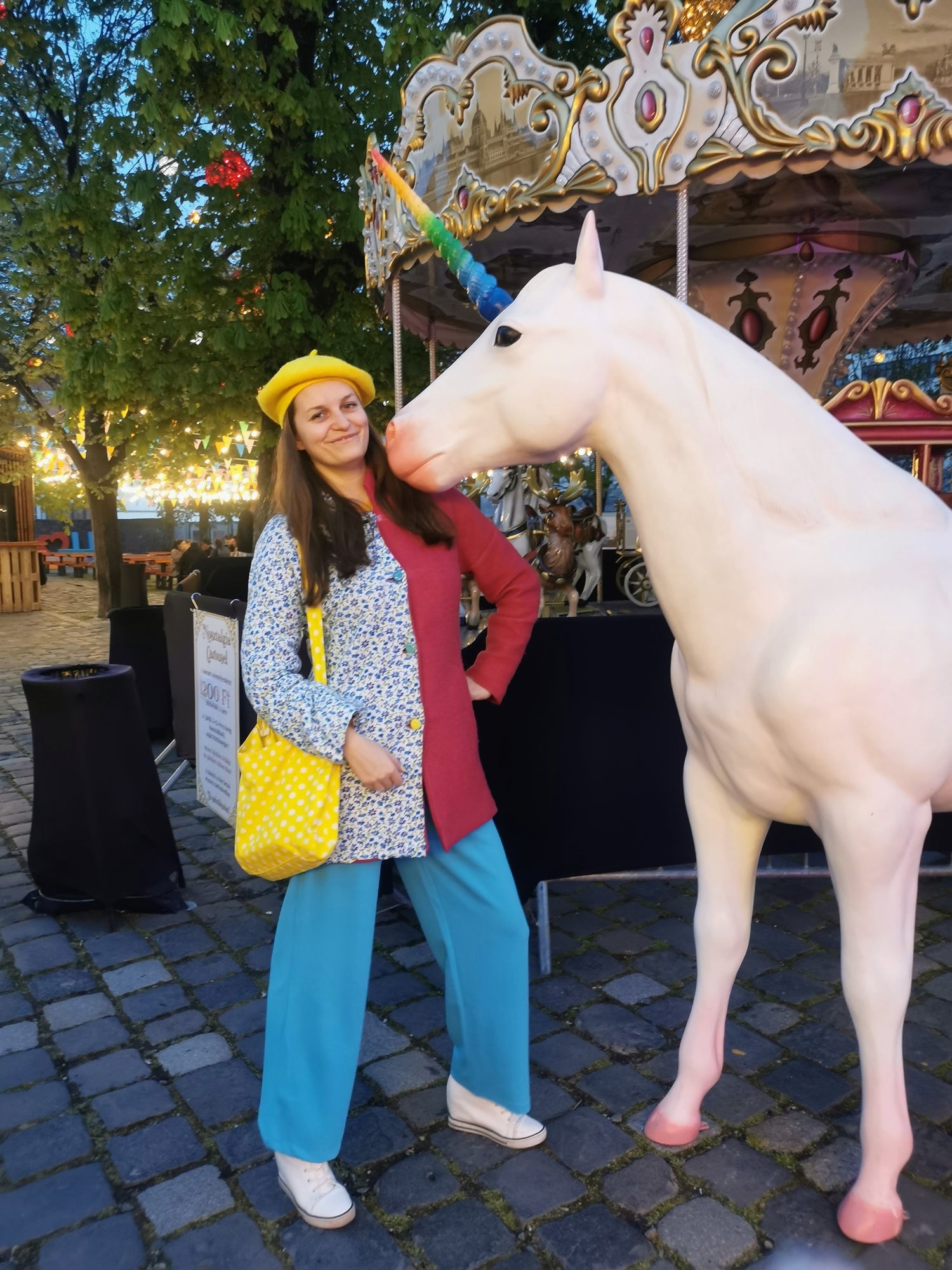 Girl wearing colorful clothes - blue pants, pink and blue coat, yellow beret and a yellow bag, unicorn is next to her. 
